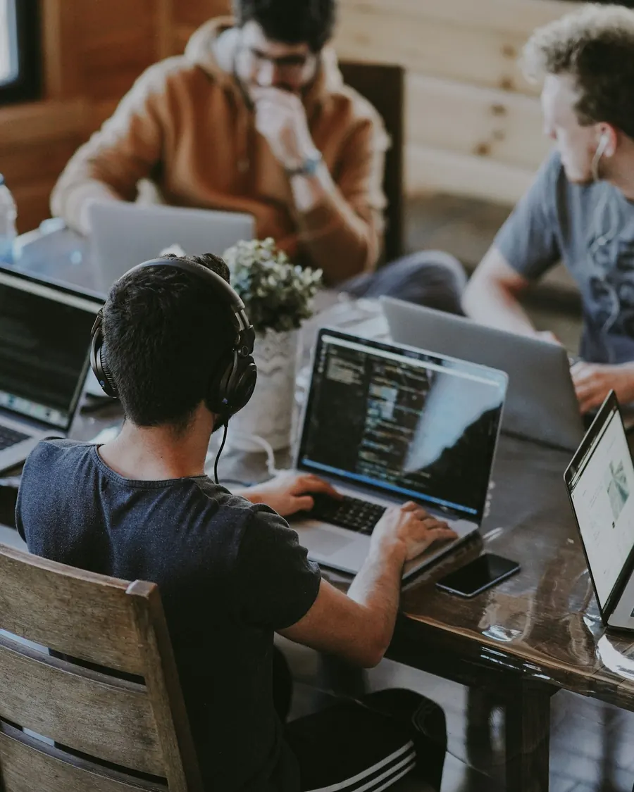 Personas programando con notebooks alrededor de una mesa de trabajo
